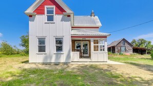 Une maison à deux étages avec un toit rouge et des murs blancs, un porche à l’avant et un petit garage attenant.