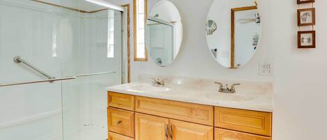 A bathroom with a glass shower enclosure, a wooden vanity with a large mirror, and a wall-mounted light fixture.