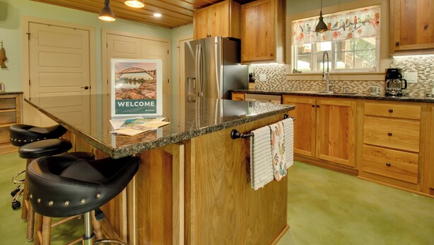 Una cocina con armarios de madera, un refrigerador de acero inoxidable, una cafetera y un letrero de bienvenida.