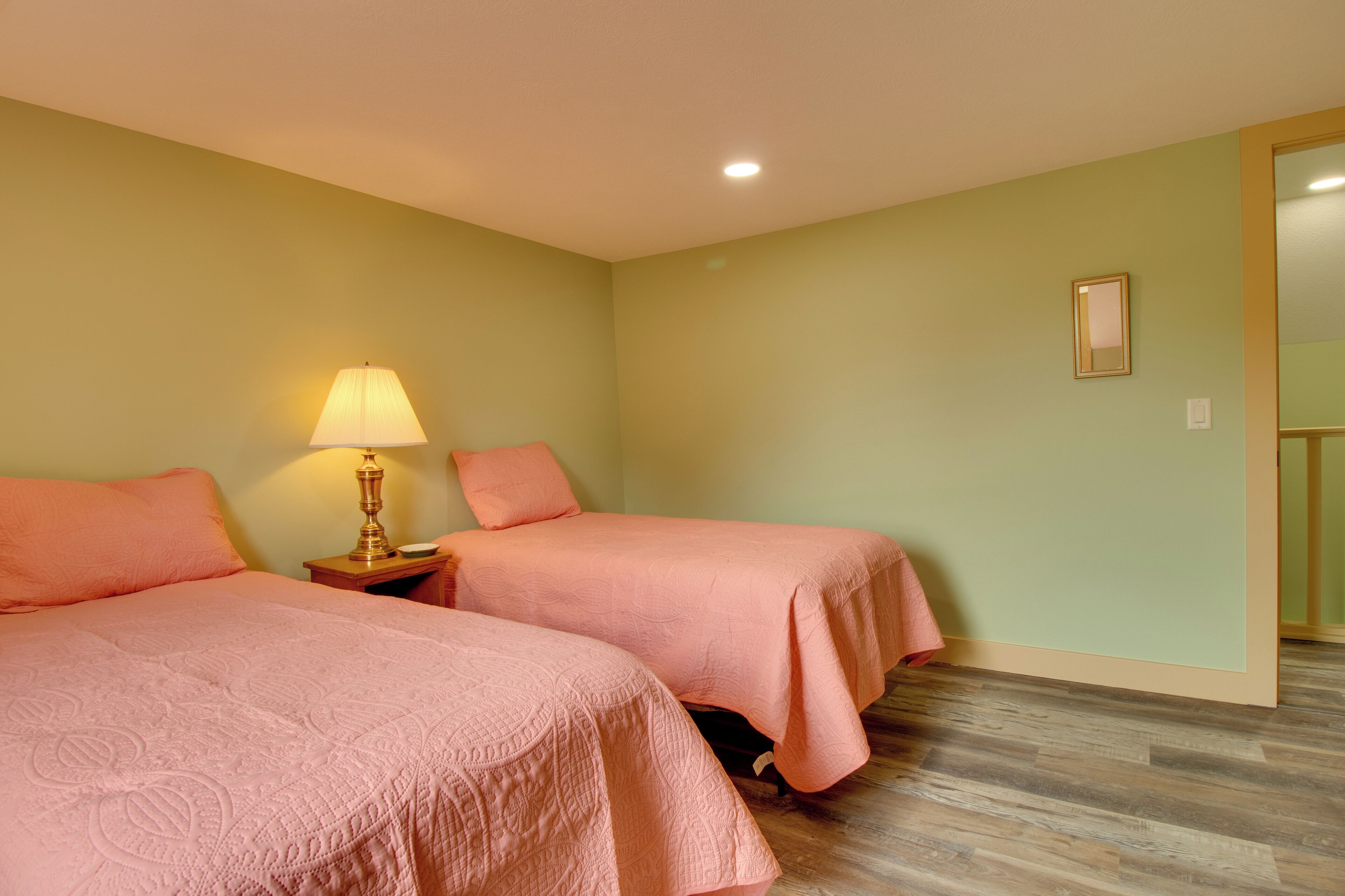 A room with two beds, a nightstand with a lamp, and a framed picture on the wall.