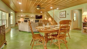 Un comedor espacioso con una mesa y sillas de madera, un ventilador de techo y una escalera que sube a un nivel superior.