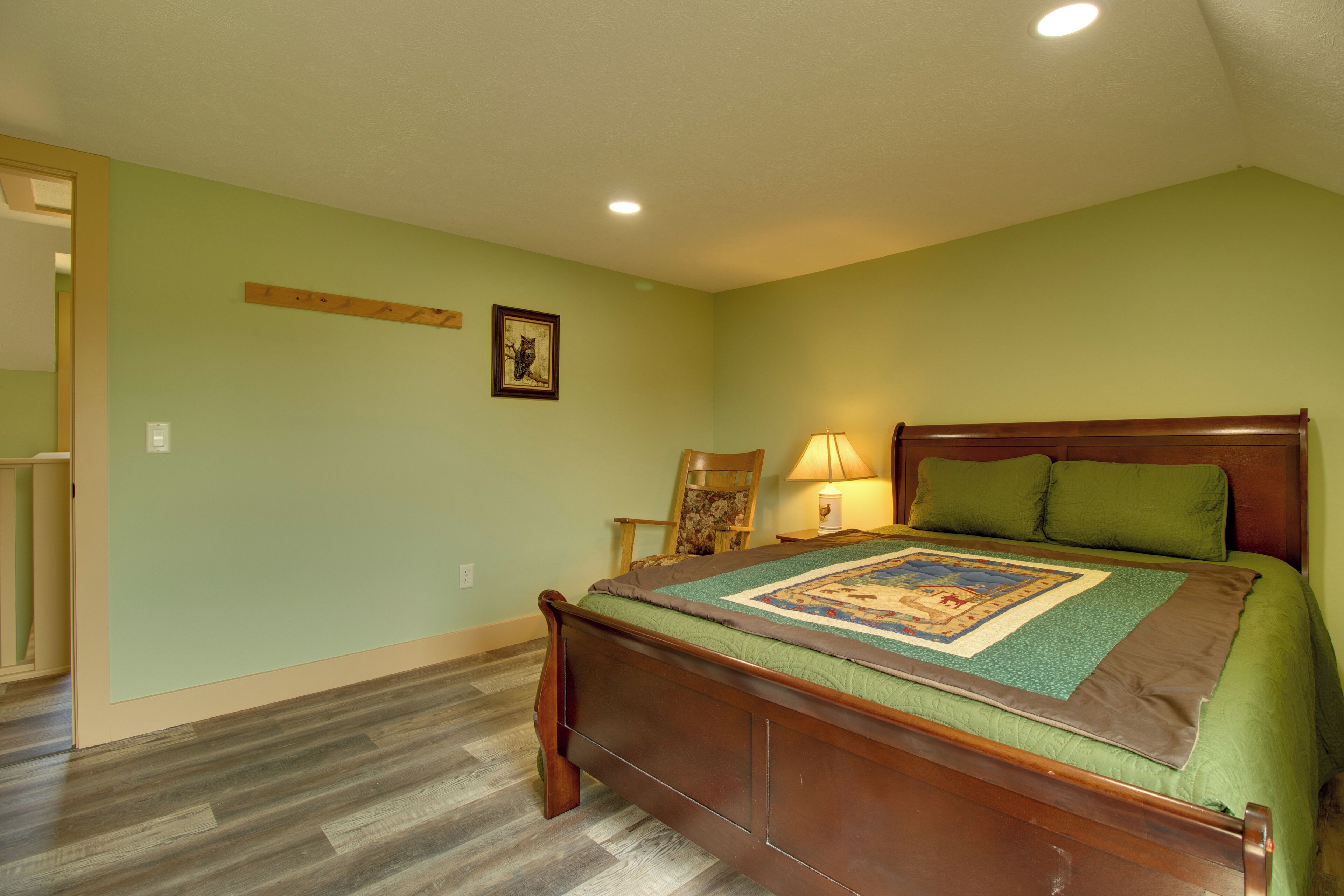 A bedroom with a wooden bed, green walls, and a wooden floor.
