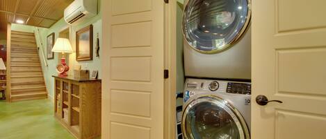A laundry room with two stacked front-loading washing machines, a wooden cabinet with baskets, and a lamp on a shelf.