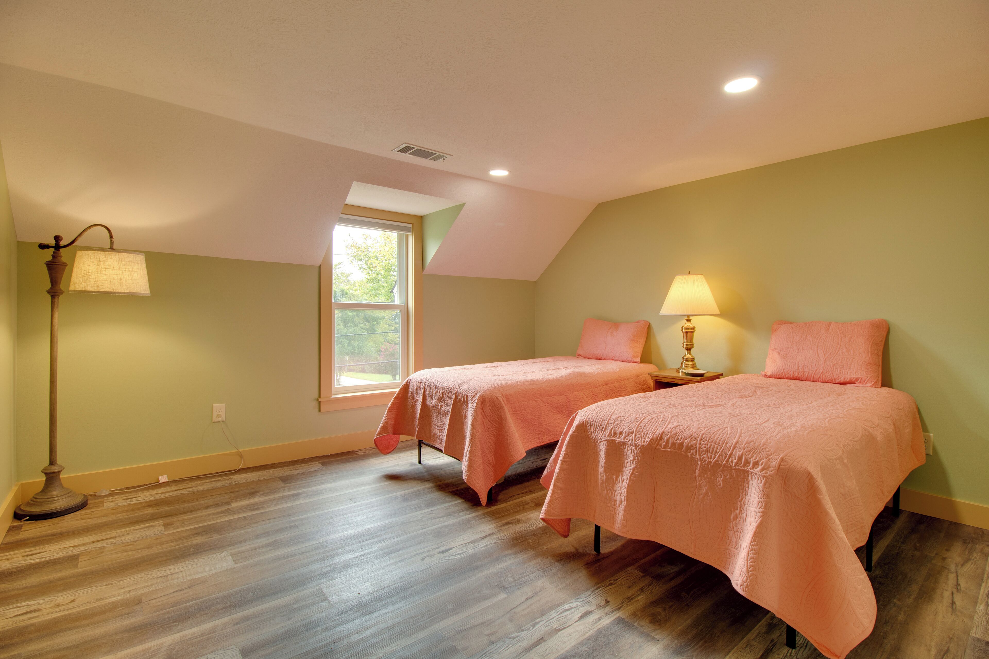 A room with two beds, a window, and a floor lamp.