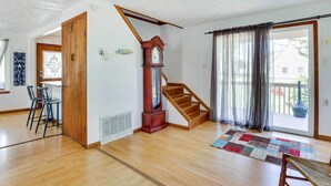 Ein geräumiges Zimmer mit einer Holztreppe, einer großen Holz-Wanduhren und Blick durch eine Schiebeglastür.