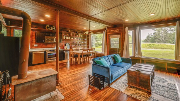 Ein rustikales Blockhaus-Interieur mit einem Essbereich aus Holz, einem blauen Sofa, einem Kamin und einer Küche mit einem 'Cafe'-Schild.
