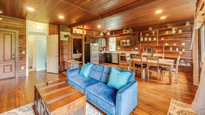 Ein großzügiger Wohnbereich mit blauem Sofa, Esstisch aus Holz und einer Küchenzeile mit Holzschränken sowie einer Kaffeestation.