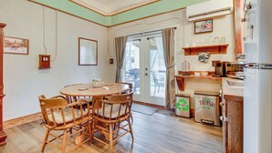 Un coin repas avec une table ronde et quatre chaises, une cuisine équipée d’un réfrigérateur et d’un évier, et une porte donnant sur l’extérieur.