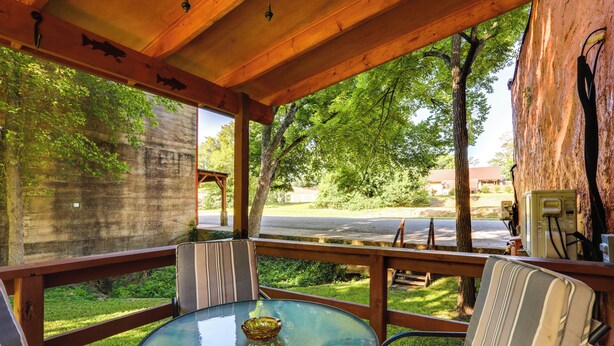 Un espace extérieur abrité, avec une table en verre et des chaises à rayures, donnant sur une route et des espaces verts.