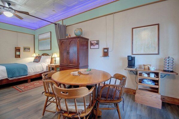 Una habitación con una cama, una mesa de comedor con sillas, un armario y una cafetera.