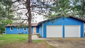 A blue house with two white garage doors, a front porch, and a tree in front. - Nisswa Lake Getaway w/ Hot Tub + Kayaks! (Nisswa)