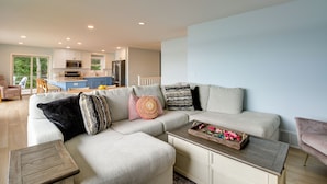 A modern living room with a sectional sofa, a wooden coffee table, and a kitchen in the background. - Nisswa Lake Getaway w/ Hot Tub + Kayaks! (Nisswa)