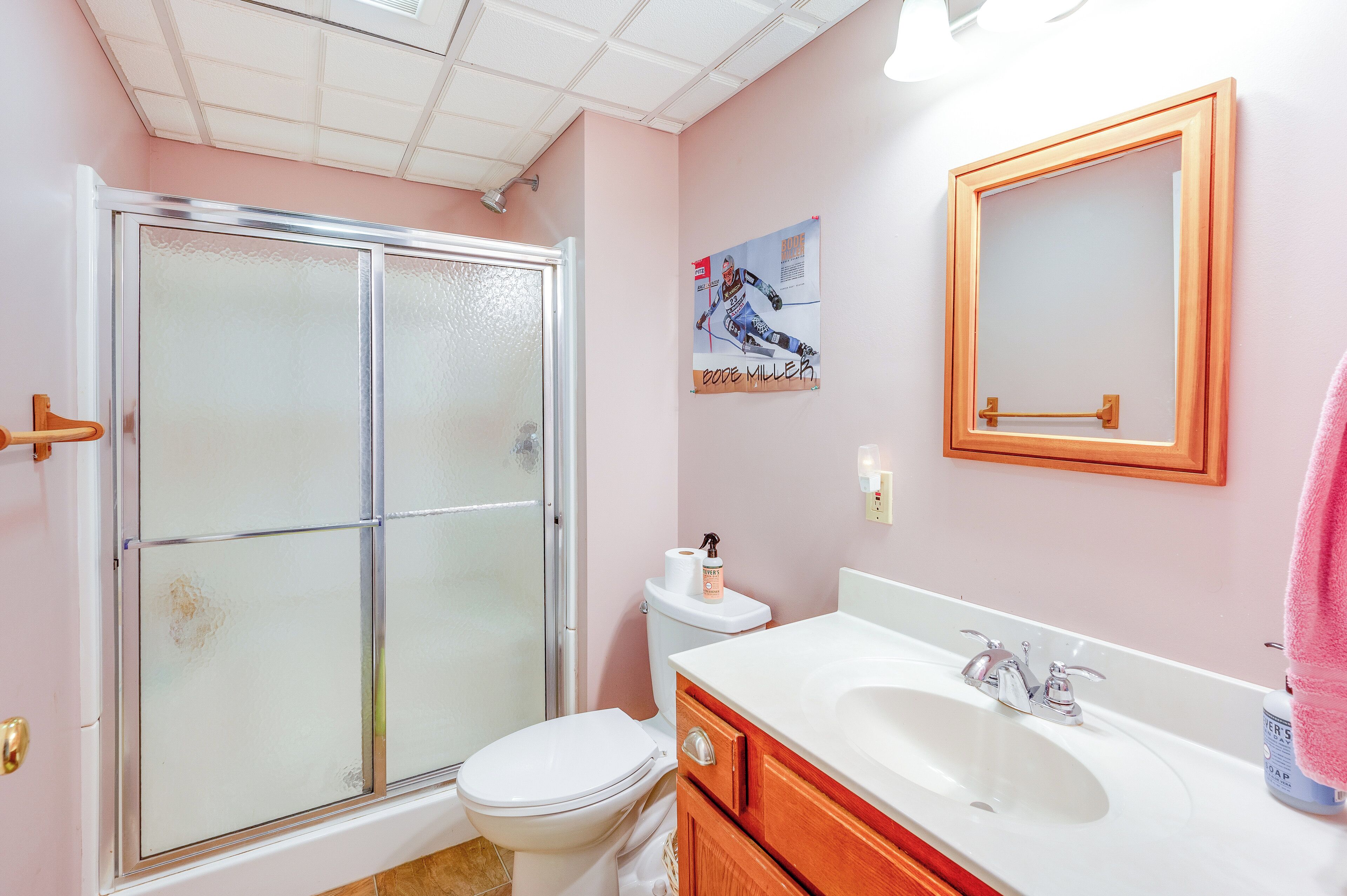 Une salle de bain avec une douche à parois de verre, des toilettes, un lavabo avec un miroir et une affiche accrochée au mur.
