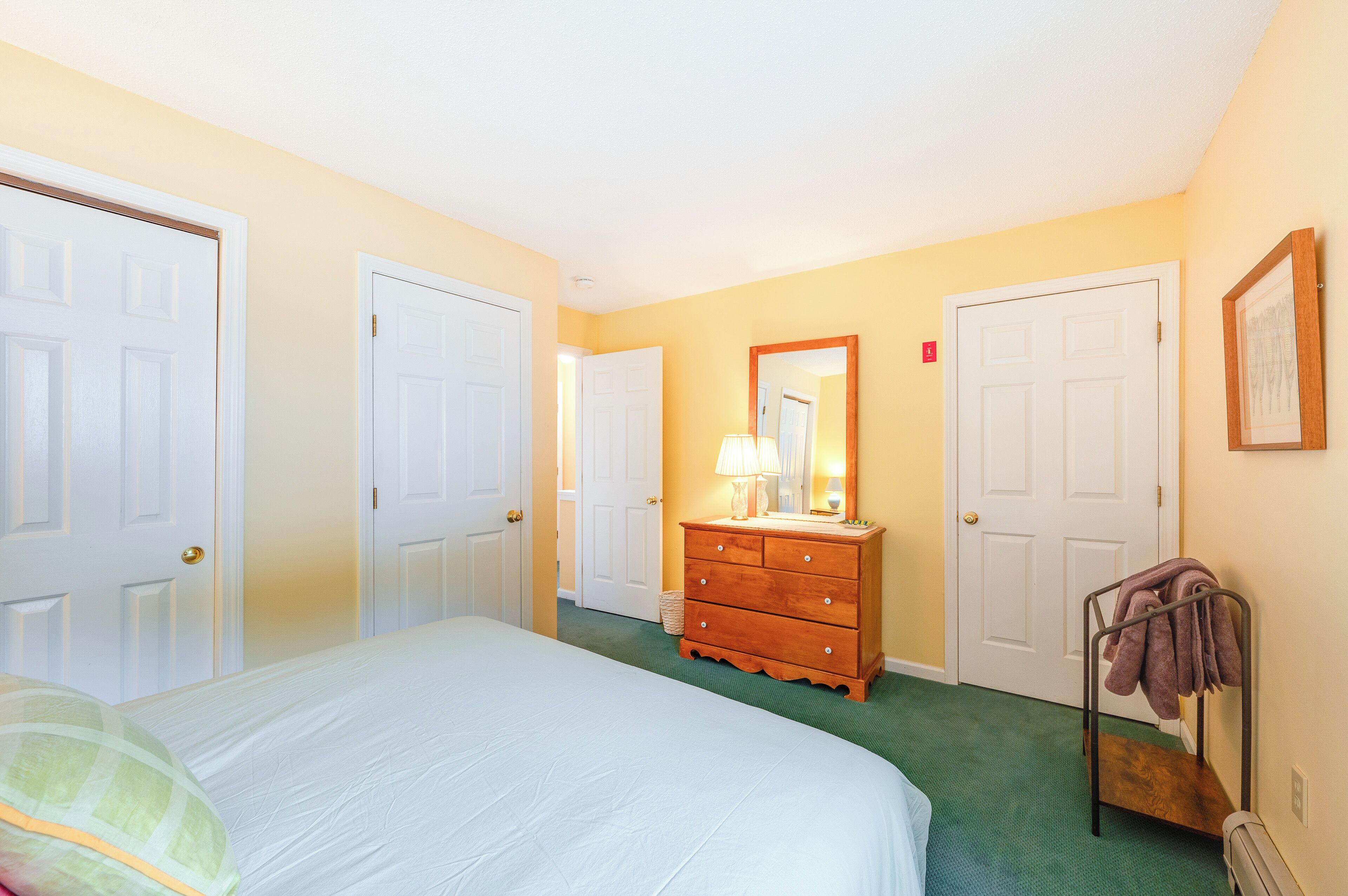 Une chambre d’hôtel avec un lit, une commode, un miroir et deux portes.