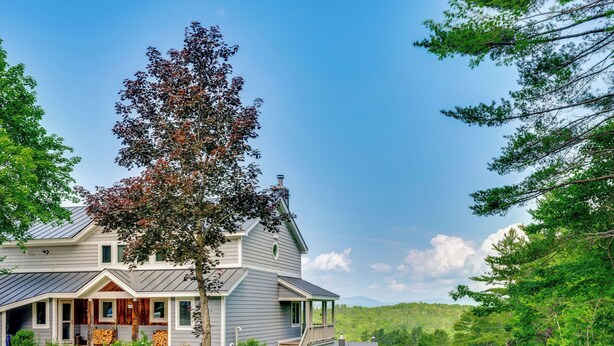 A two-story house with a covered porch, a garage, and a large tree in front.