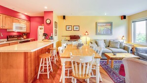 A kitchen with wooden cabinets, a microwave, and a stove. There is a dining area with a wooden table and white chairs. A sofa and a lamp are in the living area.