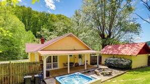 A yellow house with a red roof, a wooden deck, and a hot tub.