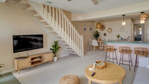 Ein modernes Wohnzimmer mit Treppe, Fernseher, Essbereich und Küche.