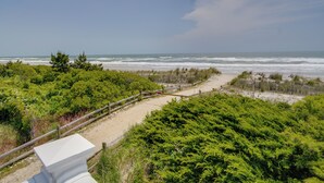 Ein Küstenpfad, der zum Strand führt, gesäumt von üppiger Vegetation und einem Holzzaun.