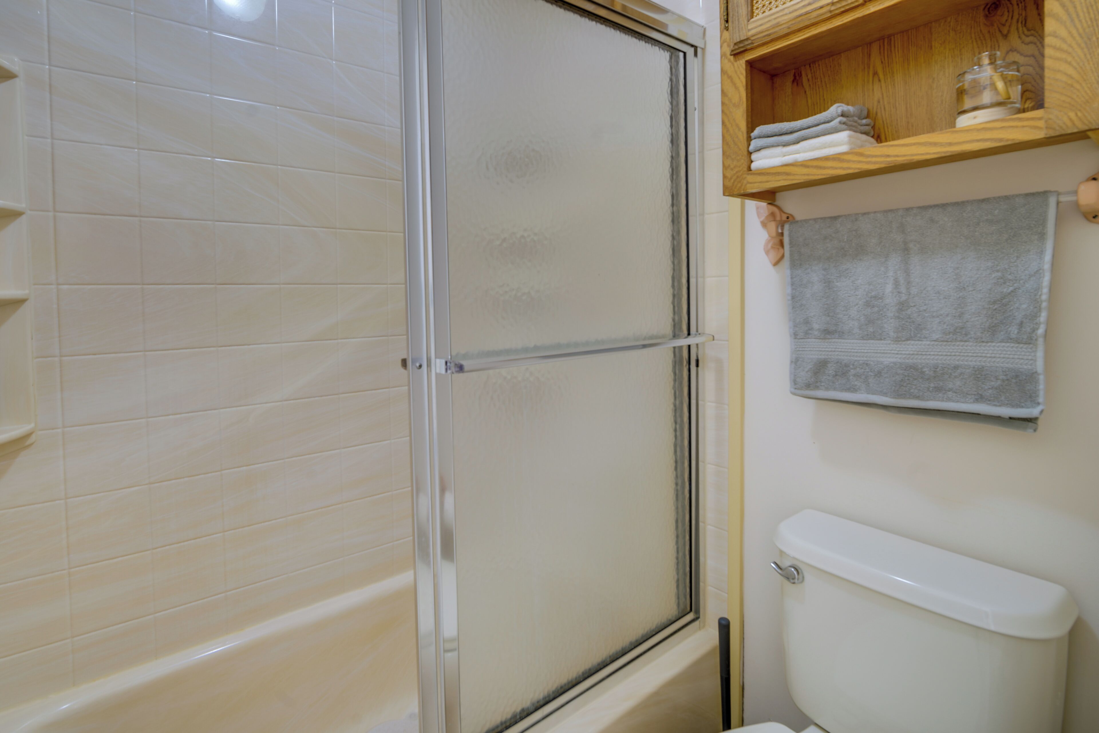 A bathroom with a glass shower enclosure, a white toilet, and a shelf with folded towels.