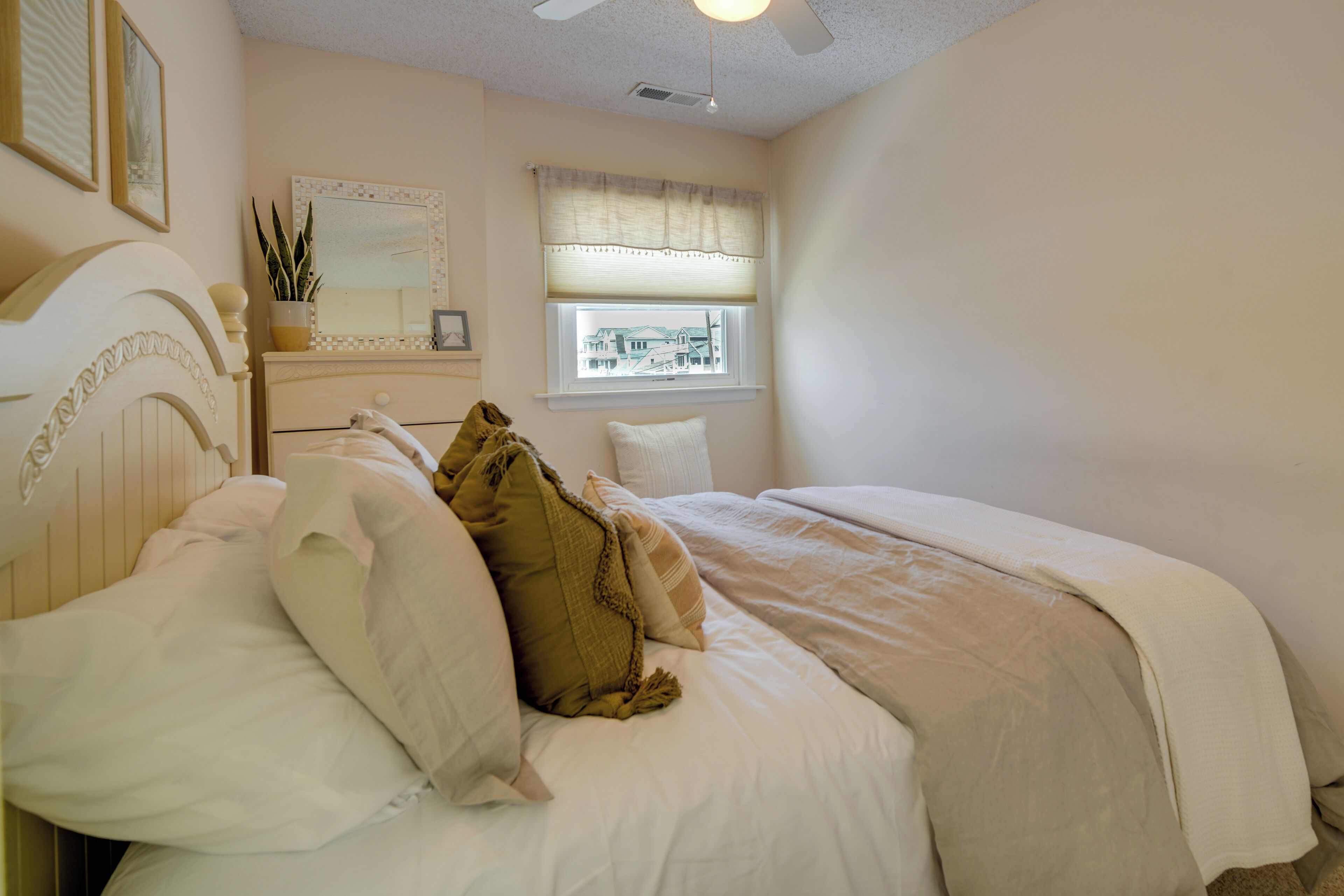 A bedroom with a bed, a dresser, a mirror, and a window with a view of a building.