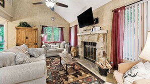 Ein gemütliches Wohnzimmer mit Kamin, Deckenventilator und Wand-Fernseher.
