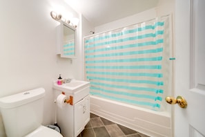 A bathroom with a toilet, sink, vanity, and bathtub. - Charming Lake Erie Cottage on Main Strip! (Geneva)