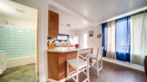 A compact kitchen with wooden cabinets, a white countertop, and a built-in sink. There are two white chairs around the counter. - Charming Lake Erie Cottage on Main Strip! (Geneva)