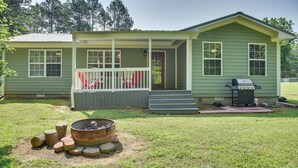 A small, single-story house with a porch, a fire pit, and a grill in the yard. - Guntersville Lake House: Dock & Boat Ramp Access! (Scottsboro)