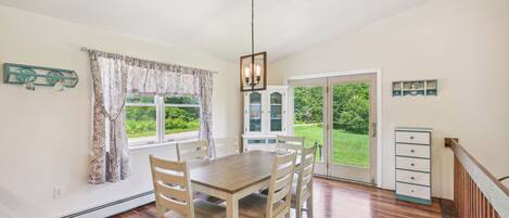 A dining area with a wooden table and chairs, a chandelier, a cabinet, and a view of greenery through a glass door.