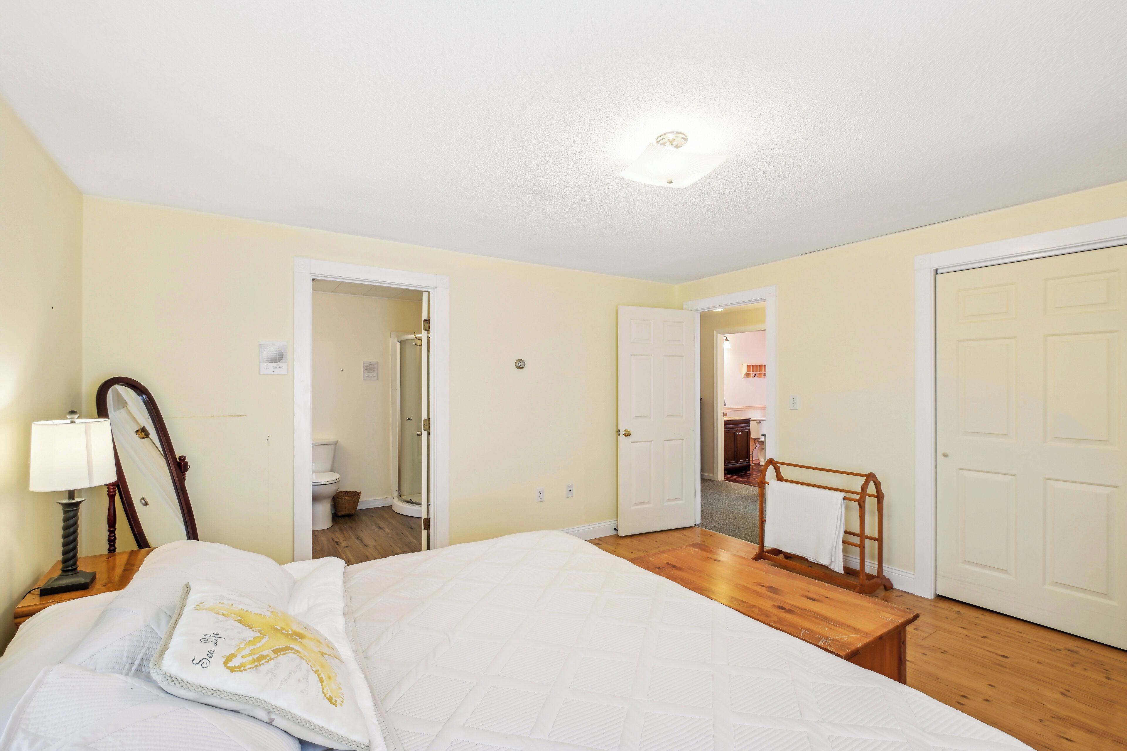 Una camera da letto con un letto, un comodino, una lampada e uno specchio. Sono presenti due porte che conducono ad altre stanze.