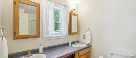 A bathroom with two sinks, wooden cabinets, a toilet, and a window with curtains.