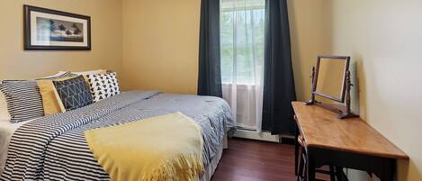 Une chambre à coucher avec un lit, une table de chevet, un miroir et une fenêtre avec des rideaux.
