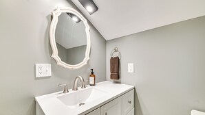 A bathroom with a white vanity, a large mirror with lighted edges, a towel ring, and a bottle of soap. - Old Forge Studio: Close to Lakes & Hiking Trails (Old Forge)