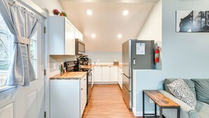 A compact kitchen with white cabinets, a microwave, and a refrigerator. There's a wooden countertop, a bench, and a sofa with a patterned pillow. - Old Forge Studio: Close to Lakes & Hiking Trails (Old Forge)