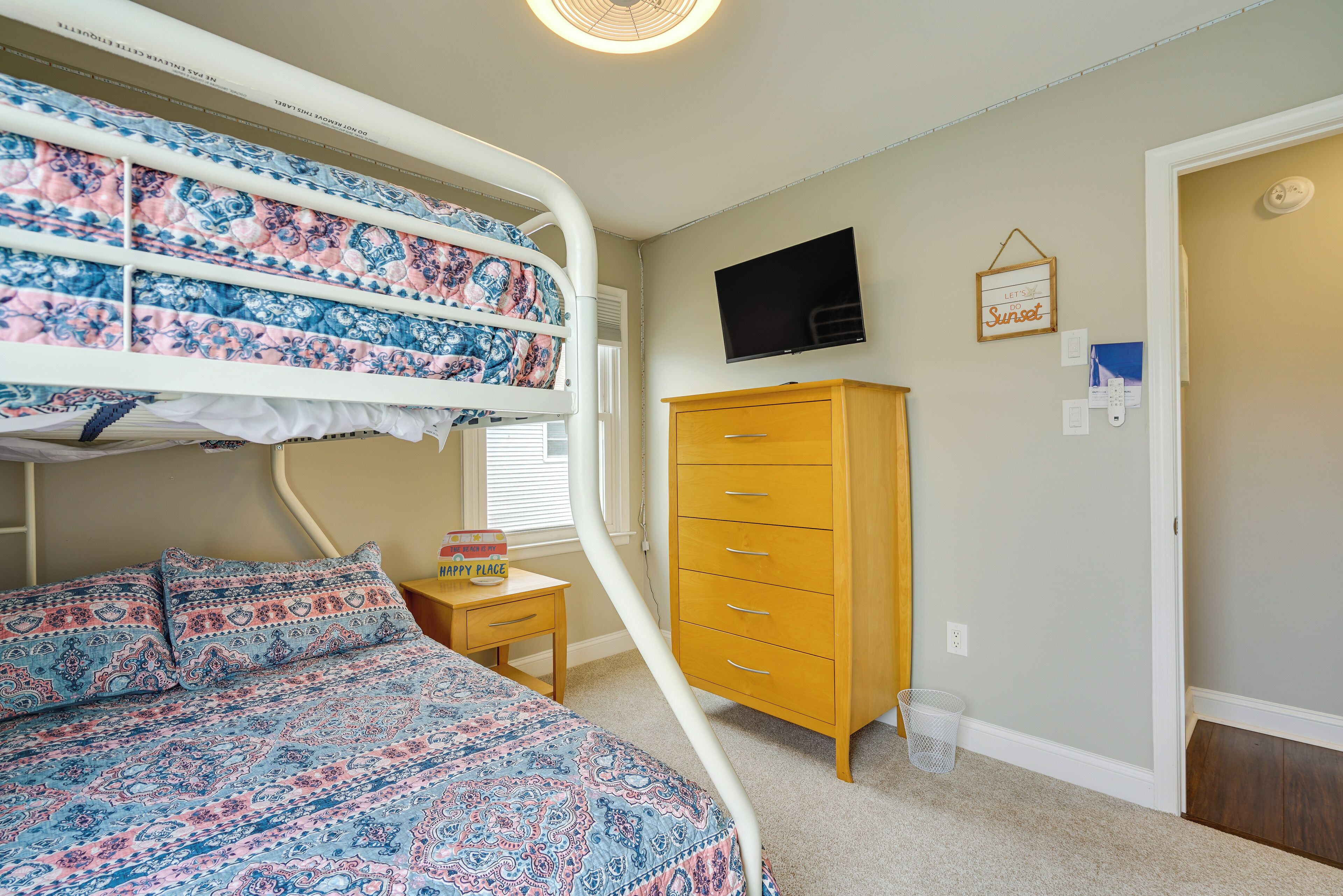 A bedroom with a bunk bed, a wooden dresser, a television, and a wall-mounted light fixture.