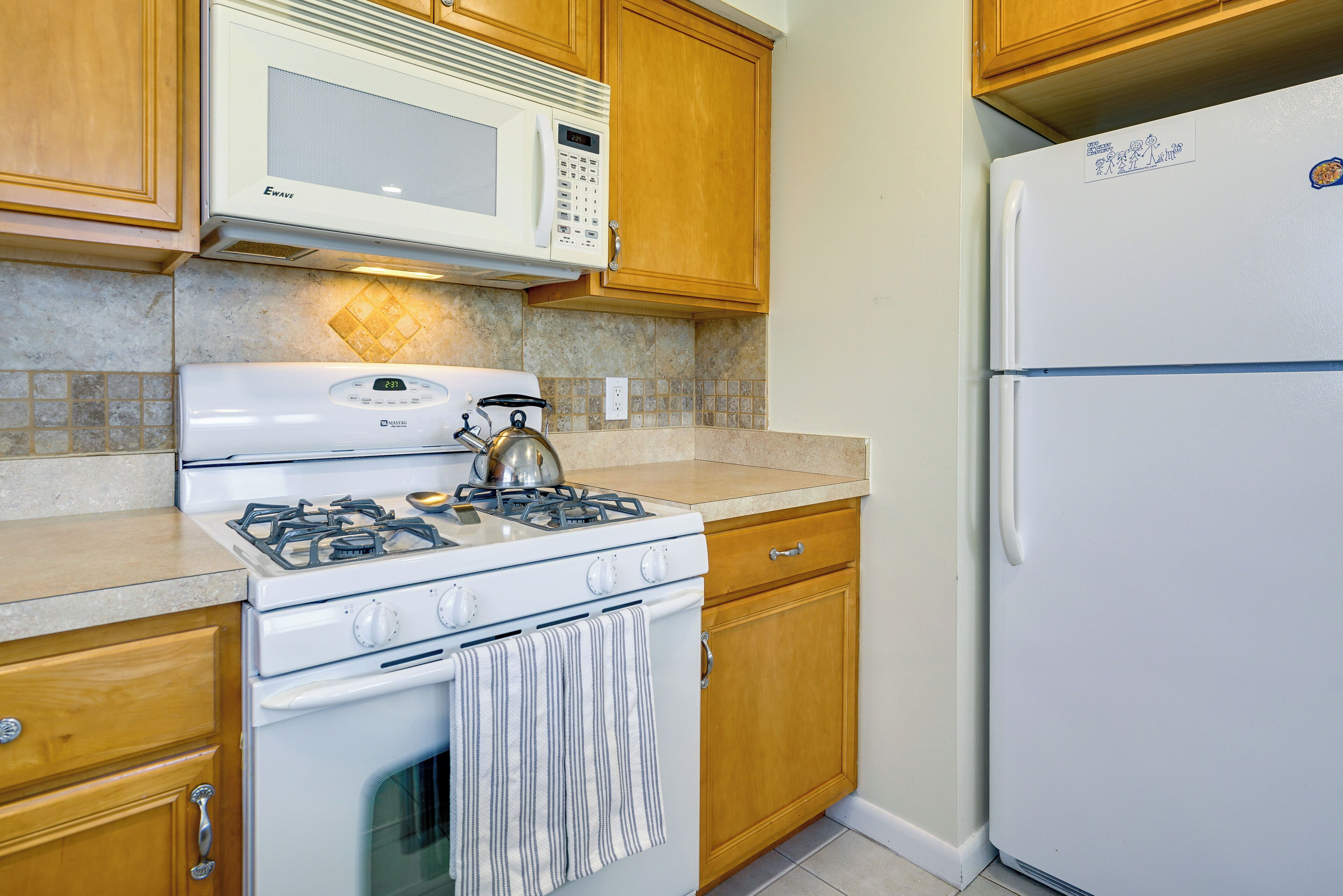 A kitchen with wooden cabinets, a white stove, a microwave, and a refrigerator.