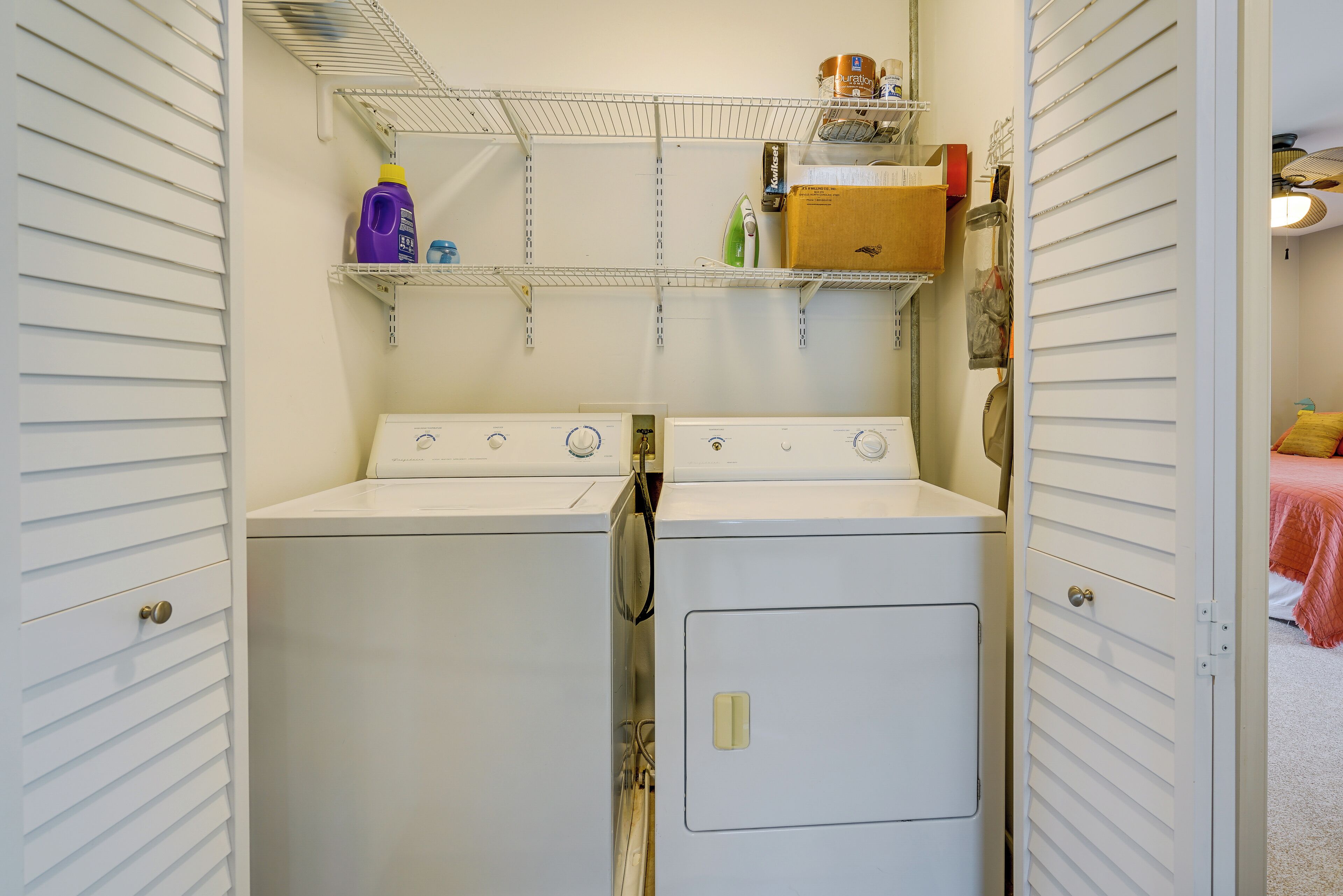 A laundry room with two washers and dryers, a shelf with cleaning supplies, and a wooden box.