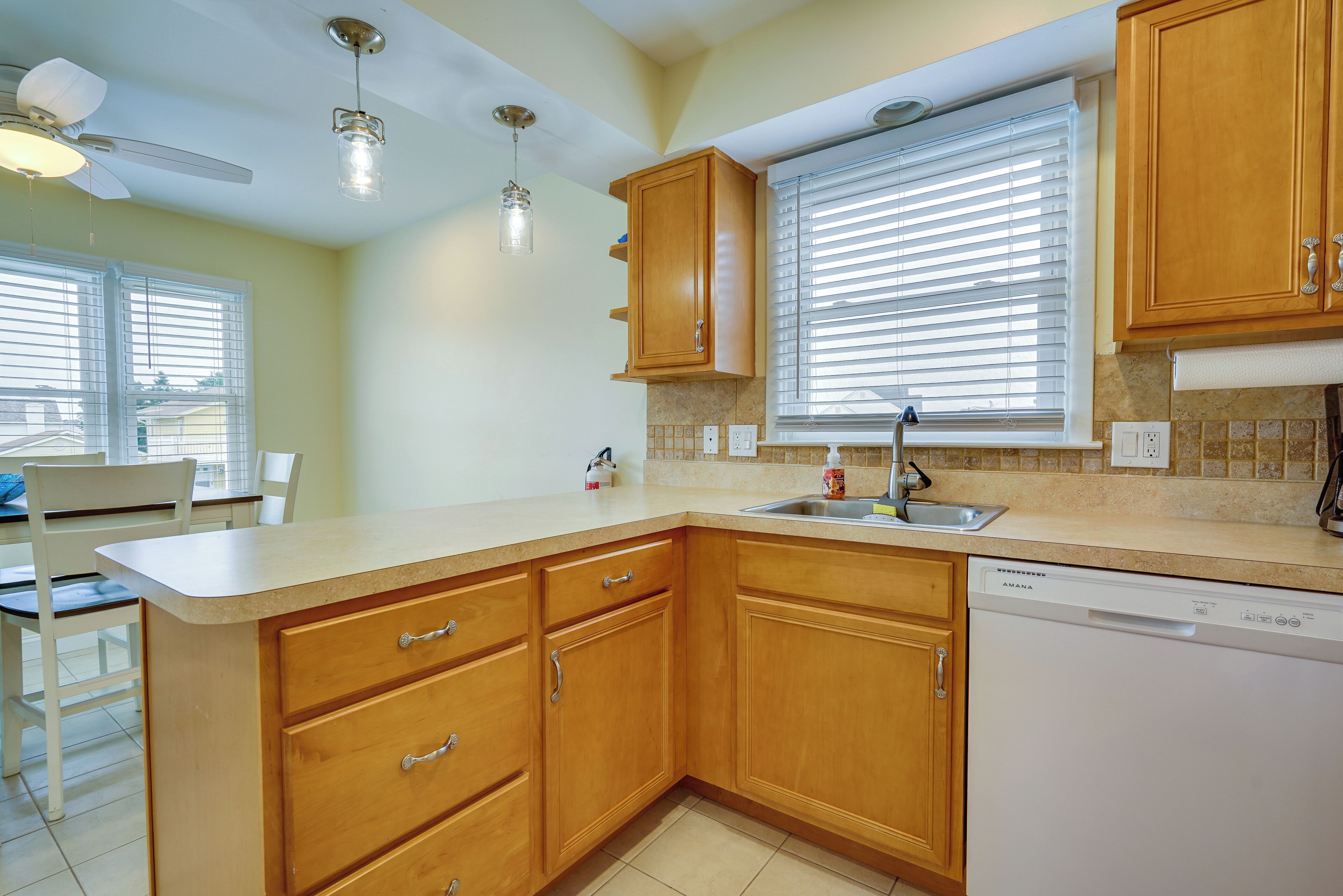 A kitchen with wooden cabinets, a dishwasher, a window with blinds, and a ceiling fan.