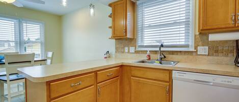 A kitchen with wooden cabinets, a dishwasher, a window with blinds, and a ceiling fan.