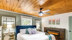A bedroom with a wooden ceiling, a bed with a blue headboard, a fireplace, and artwork on the wall. - Lindale Vacation Rental w/ Deck & Grill! (Lindale)
