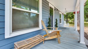 A porch with a wooden chair and a bench, a window with blinds, and a hanging planter with flowers. - Lindale Vacation Rental w/ Deck & Grill! (Lindale)