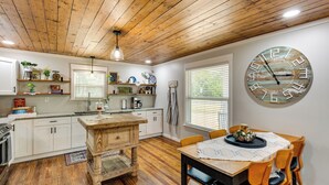 A kitchen with wooden cabinets, a wooden dining table, and a large clock on the wall. - Lindale Vacation Rental w/ Deck & Grill! (Lindale)