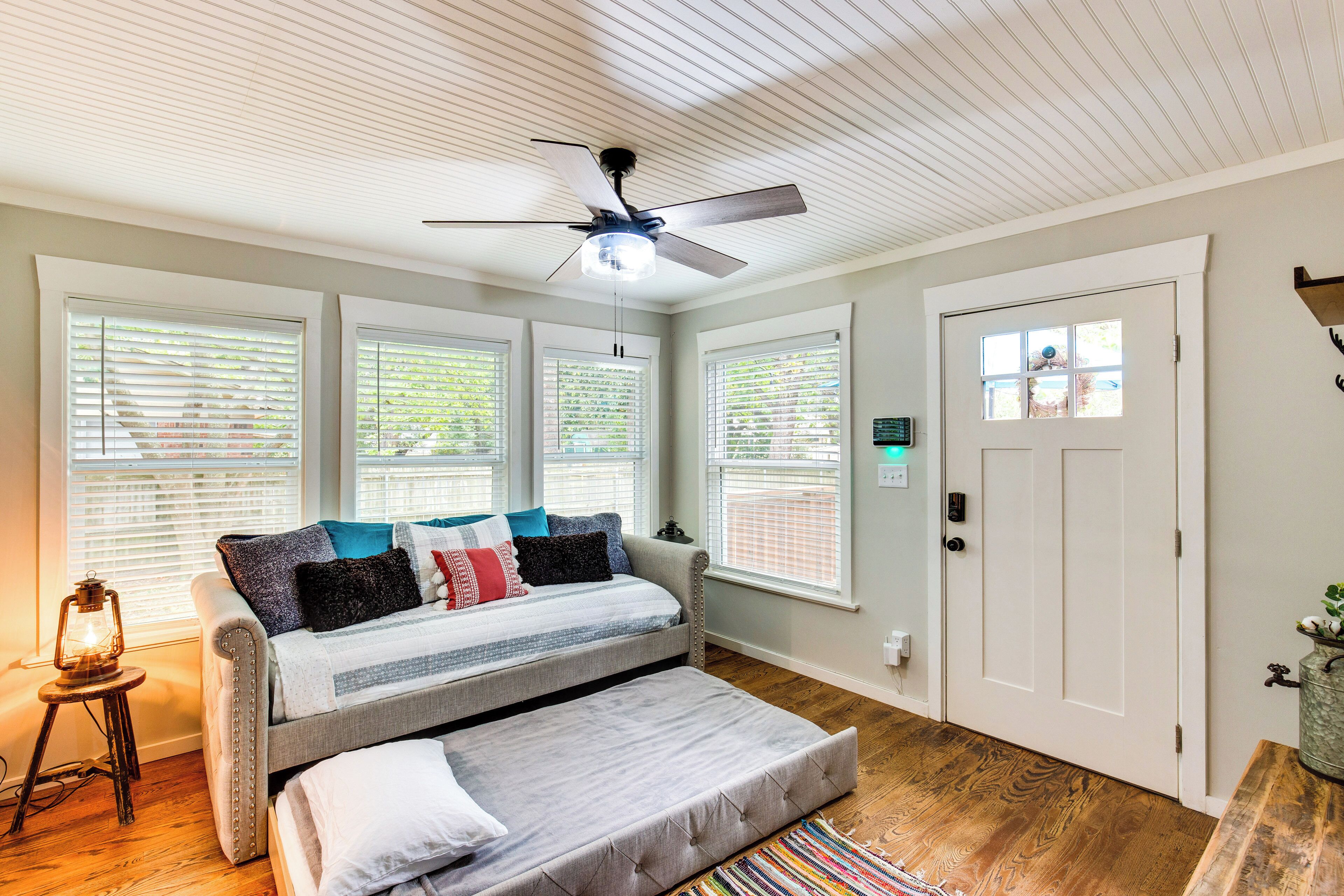 A room with a bed, a ceiling fan, and large windows with blinds.