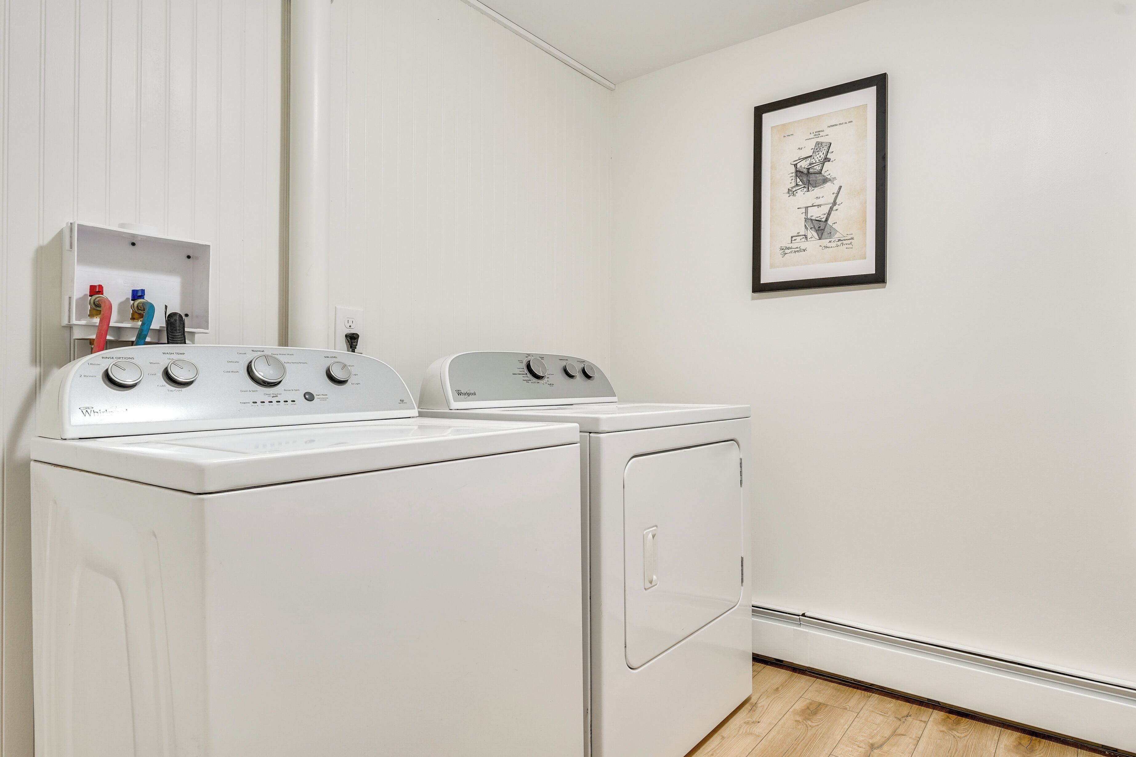 Une buanderie avec deux machines à laver et deux sèche-linge blancs, un mur blanc et un dessin encadré accroché au mur.