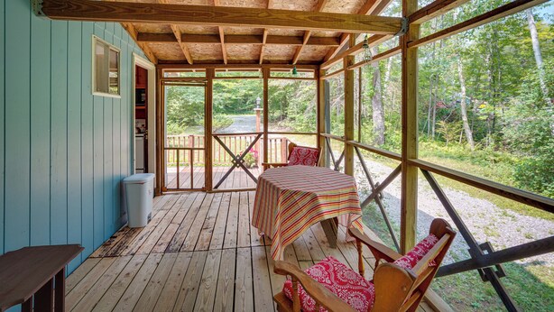 A wooden deck with a table and chairs, a window, and a view of the forest. - Cozy Becket Cottage Escape w/ Lake Access! (Becket)