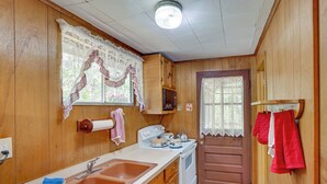 A compact kitchen with wooden walls, a white countertop, a sink, a stove, and a door with a window. - Cozy Becket Cottage Escape w/ Lake Access! (Becket)