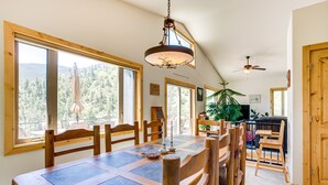 A dining area with a large wooden table, chairs, and a view of a forest through large windows. - Mountain Retreat in Drake w/ Fireplace & Views! (Drake)
