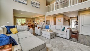 A spacious living area with a large sectional sofa, a dining table, and a kitchen in the background. - Houghton Lake Home w/ Private Dock + Kayaks! (Houghton Lake)