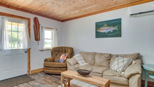 Een gezellige woonkamer met een houten plafond, een bruine leren fauteuil, een beige bank, een houten salontafel en een schilderij van vissen aan de muur.